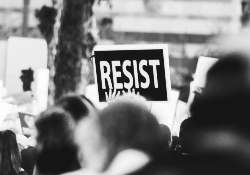 Black and white photo of a protest with a big sign saying "Resist" in white text on a black background